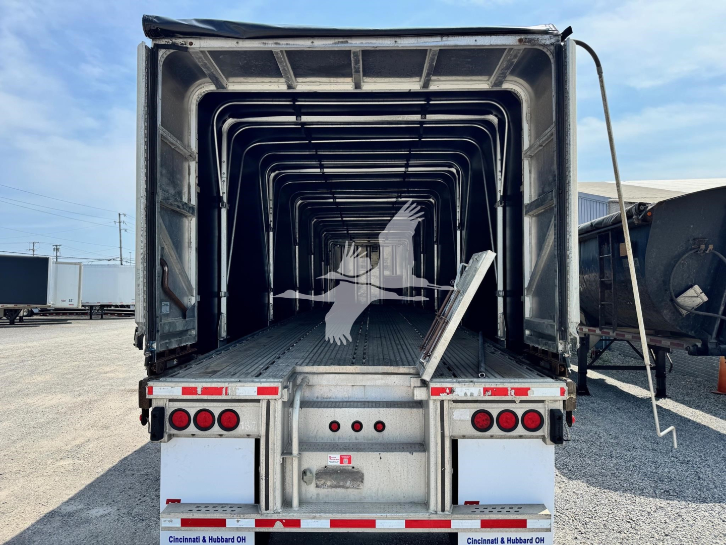Trailer bed interior showing aluminum flatbed with ribbed sides and open rear, viewed from back with tail lights and loading ramp/step visible.
