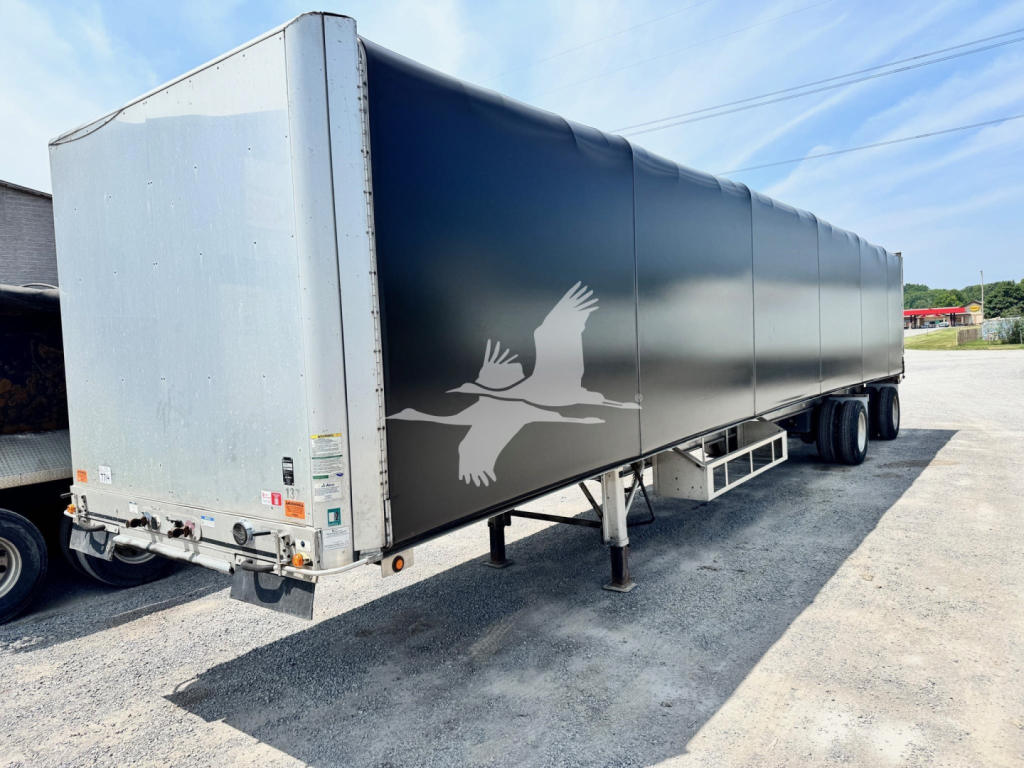 Curtainside flatbed trailer in aluminum with logo on side and dual rear axles