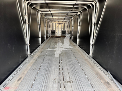 Trailer interior: aluminum curtain-side flatbed with ribbed metal floor and curved support frames forming a tunnel-like aisle.
