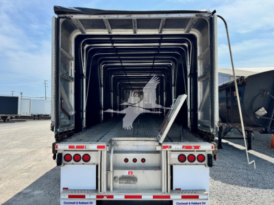 Trailer bed interior showing aluminum flatbed with ribbed sides and open rear, viewed from back with tail lights and loading ramp/step visible.