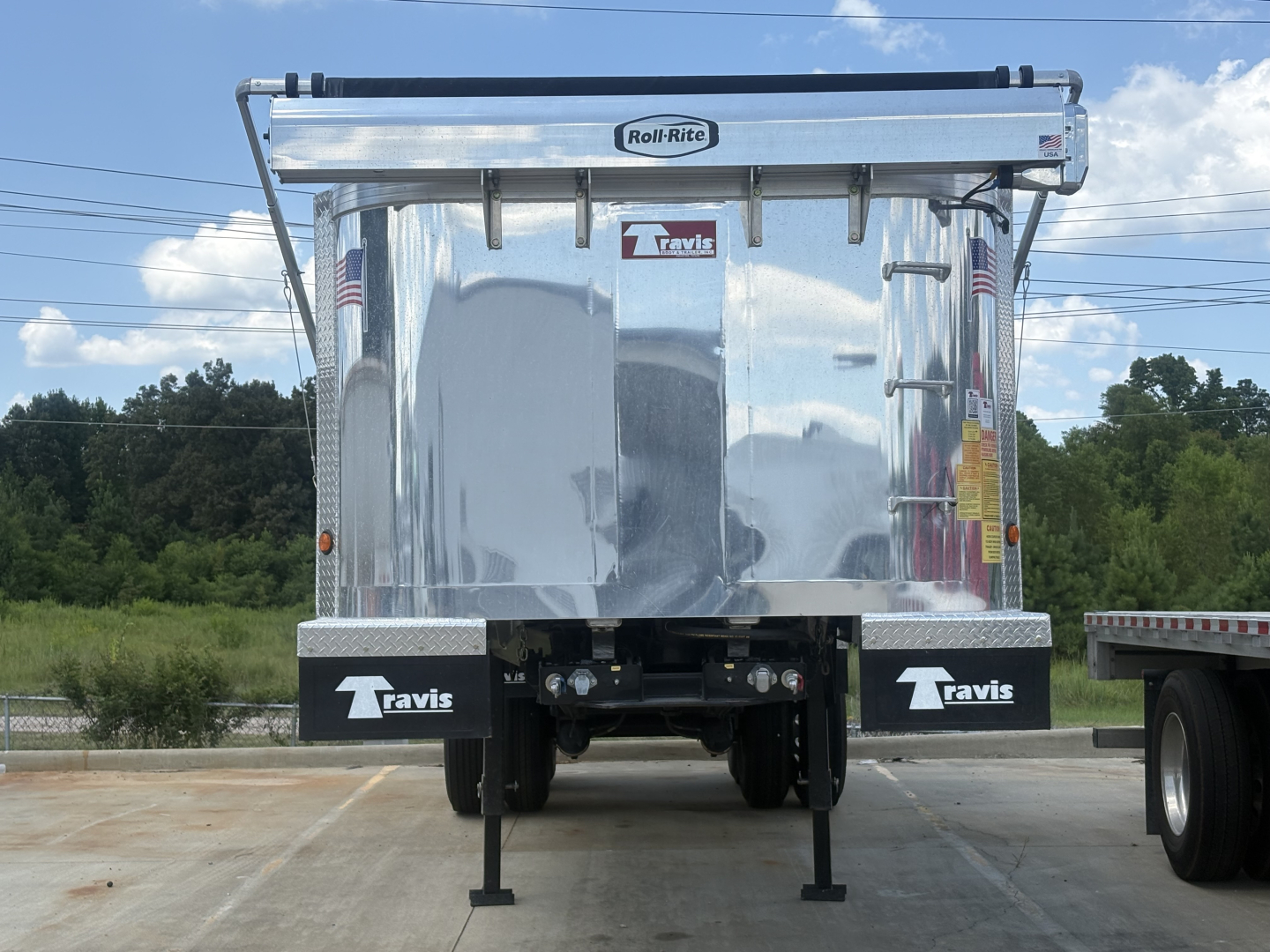 Roll-RiteEnviro roll tarp system on top of aluminum end-dump trailer with Tavis branding; back of trailer shows two stabilizer legs and bumper with Tavis logos; small stickers on the sides and a VIN/sticker area.