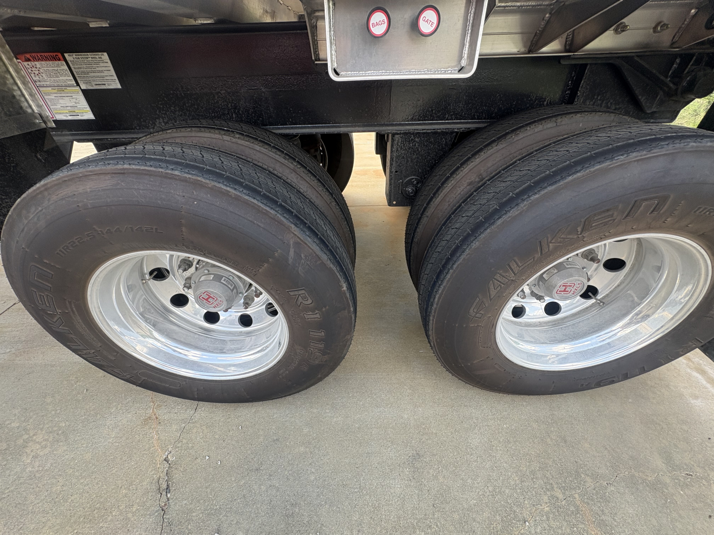 Dual rear trailer tires with polished rims under trailer frame showing tires and hubcaps