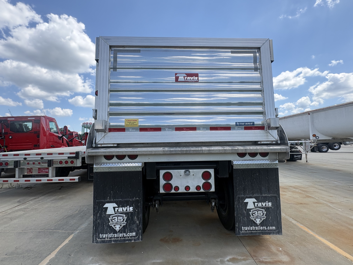 Rear view of a Travis END DUMP trailer showing stamped metal tailgate, stacked LED taillights, and dual mud flaps with Travis logo.