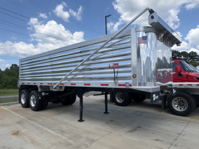 End dump trailer showing aluminum side panels and rear hoist mechanism with American flag sticker and support legs.