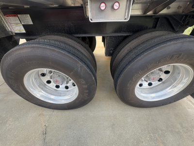Dual rear trailer tires with polished rims under trailer frame showing tires and hubcaps