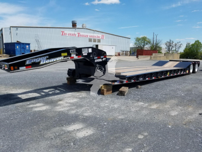 Lowboy trailer by Eager Beaver 35Gsl with black gooseneck and silver deck, labeled 35GSL-PT, parked in lot with building in background.