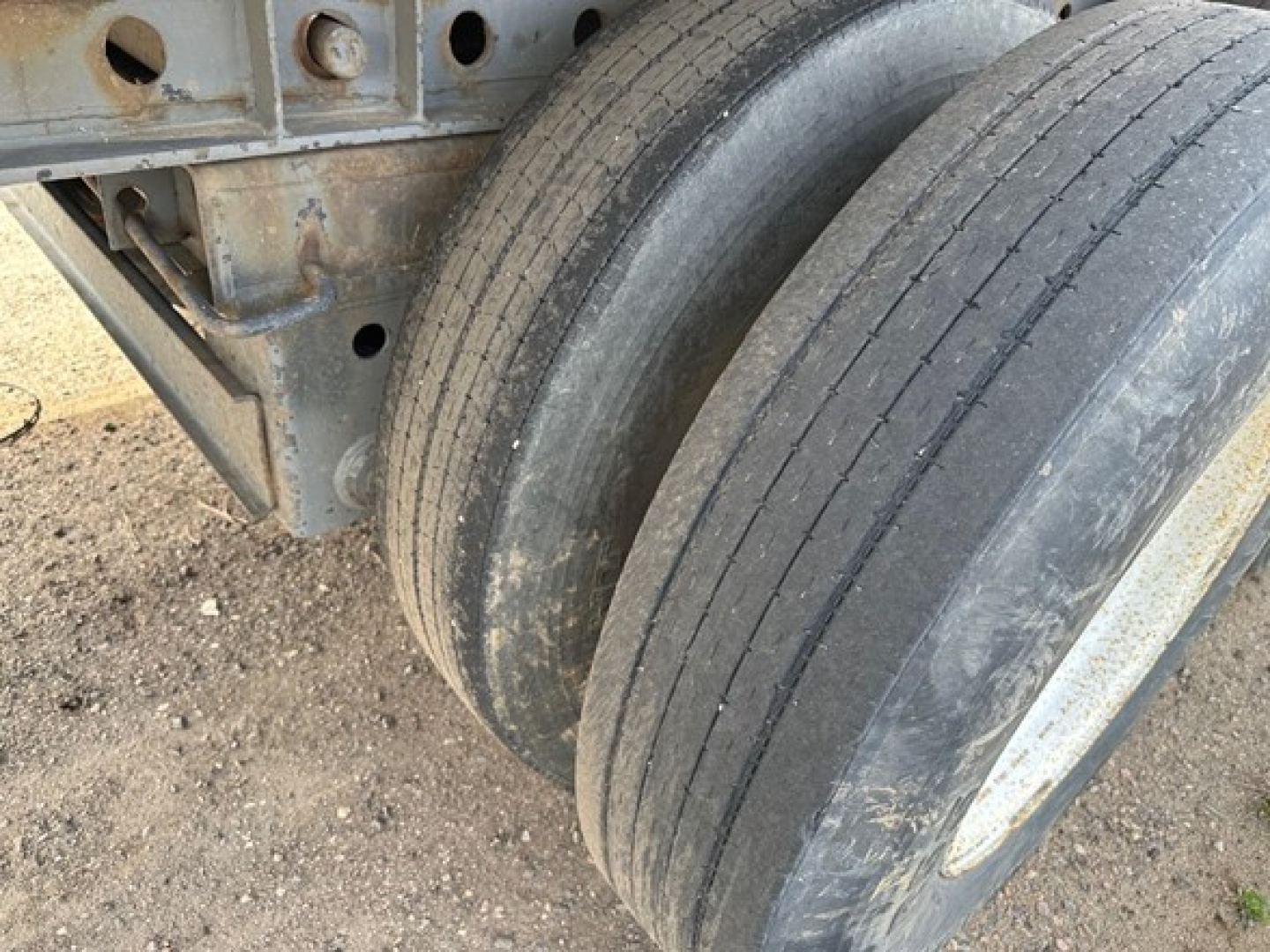 Trailer axle with dual tires and frame showing rust and wear on the steel components.