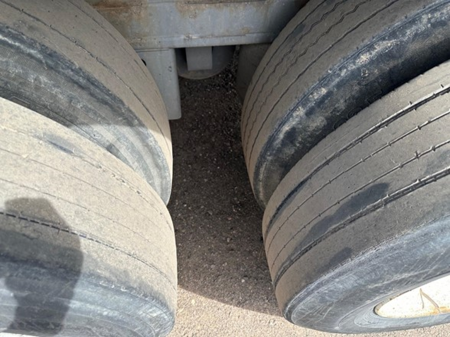 Trailer wheels and undercarriage of a Clark steel flatbed showing dual axles with worn tires and frame components.
