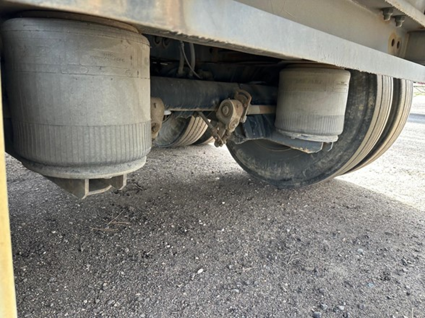 Flatbed trailer undercarriage showing dual air tanks and suspension components.