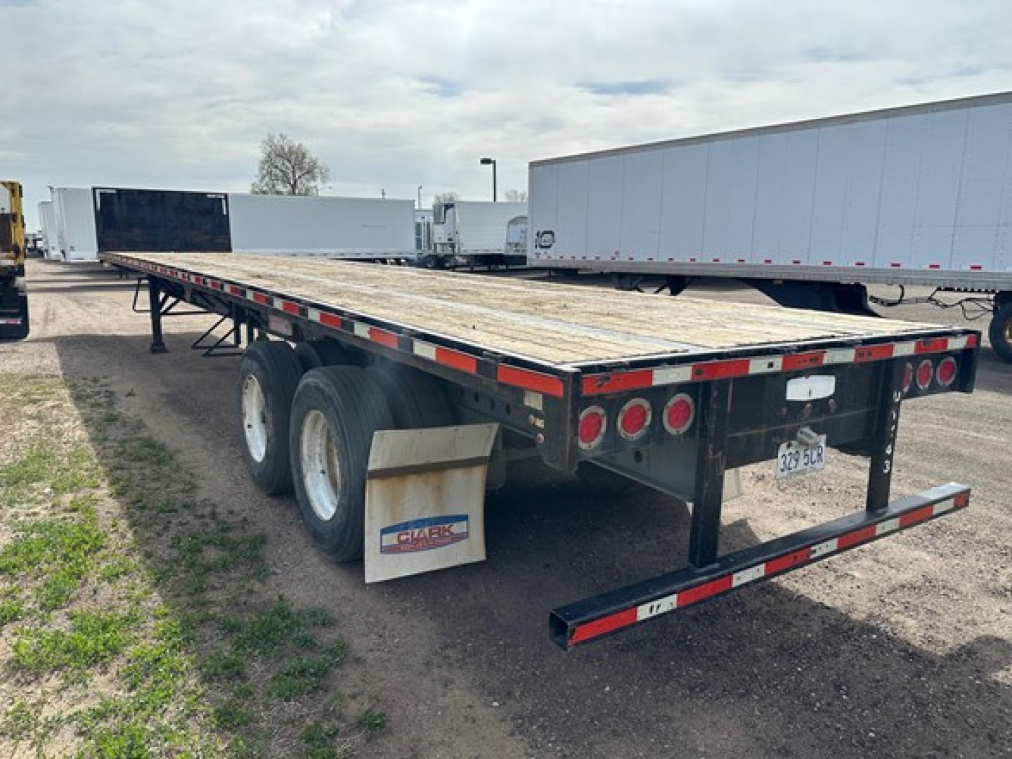 Flatbed trailer showing dual rear axles with wooden deck and mudflaps; red and white reflective tape along edges; GIABK mudflap; license plate visible at rear.