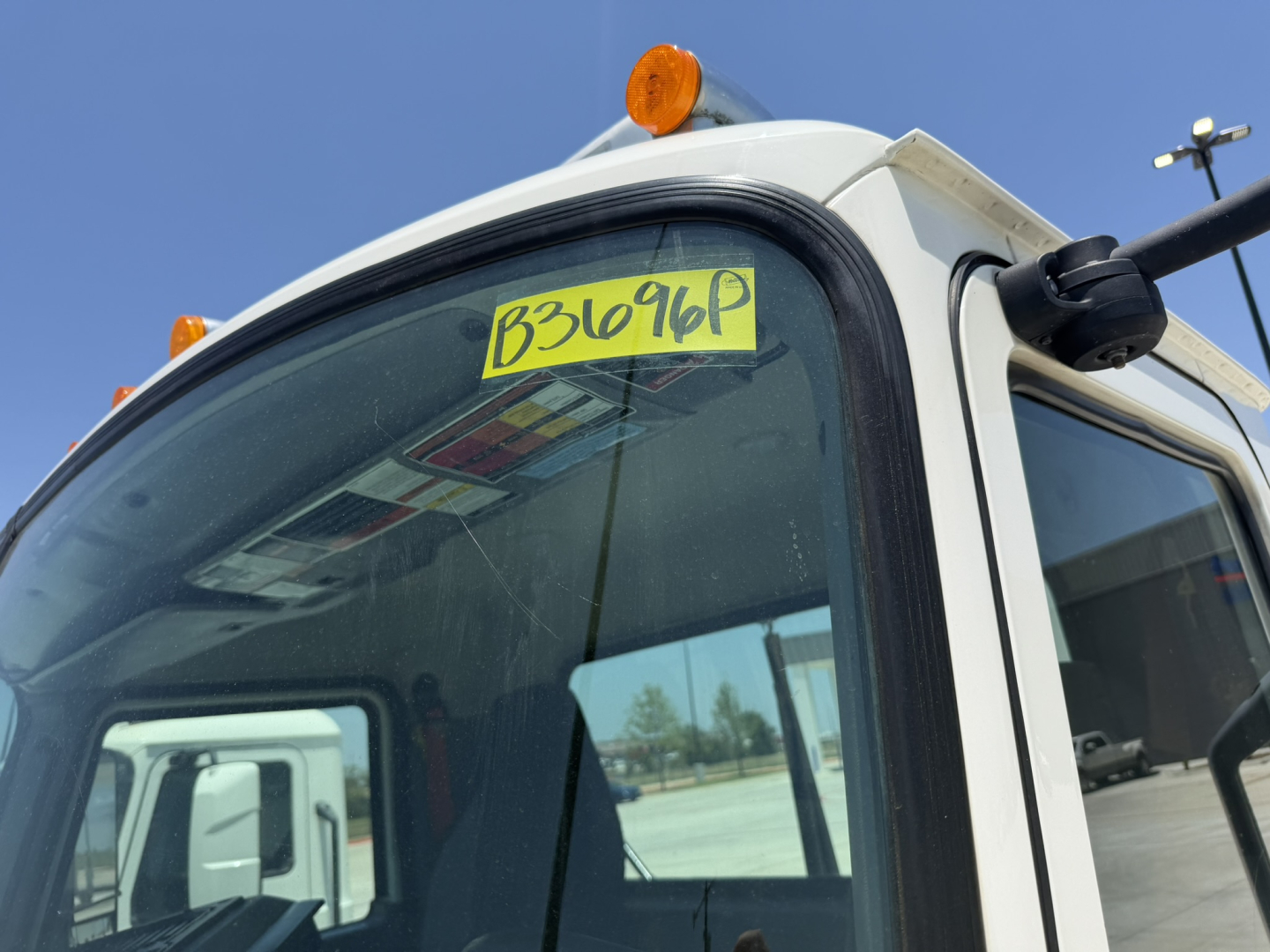 Truck cab corner with yellow inventory sticker on windshield and side mirror visible.