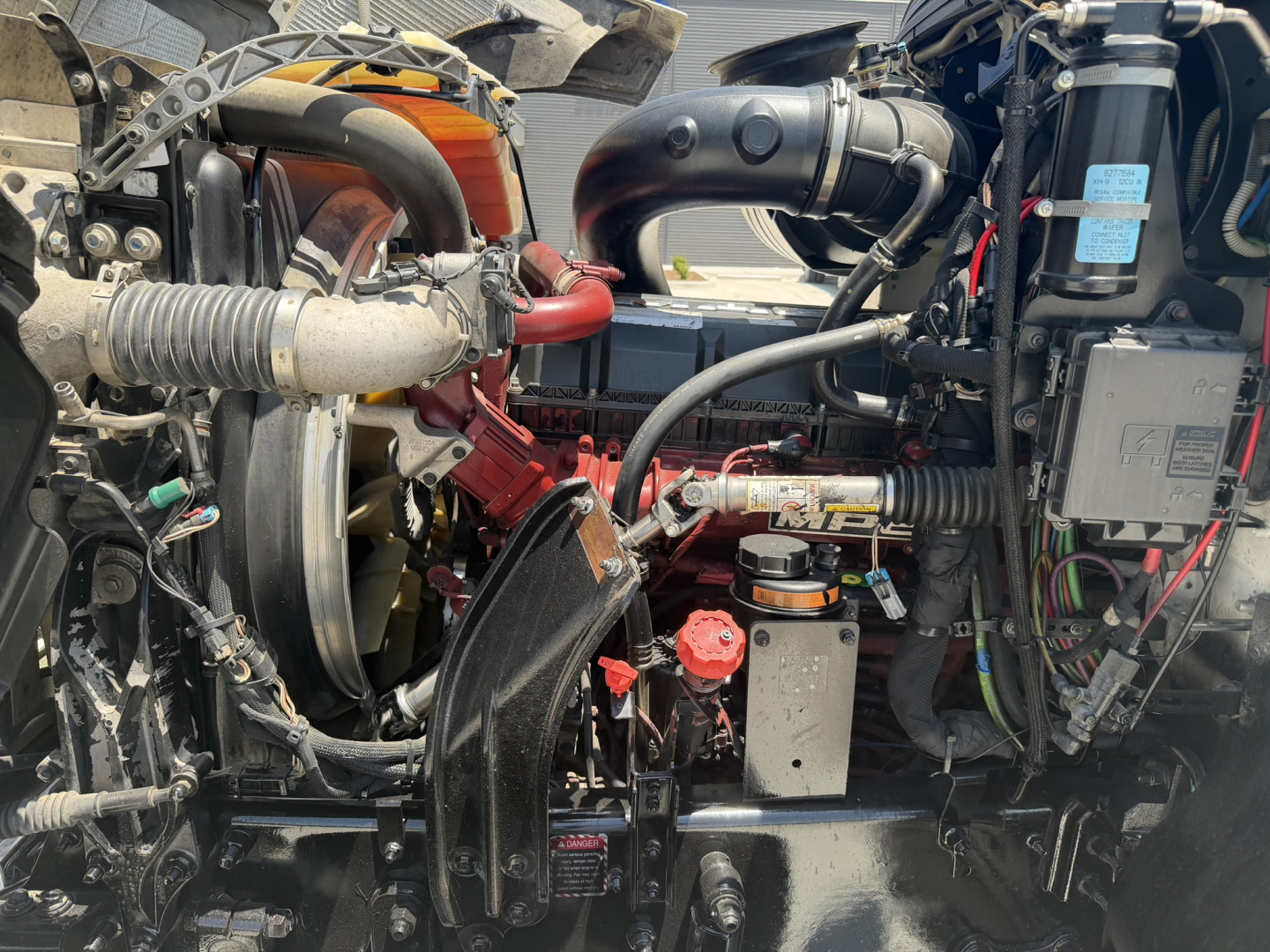 Mack PI64T engine bay showing turbocharger, hoses, electrical harness, and coolant/air intake plumbing with visible red engine components and wiring.