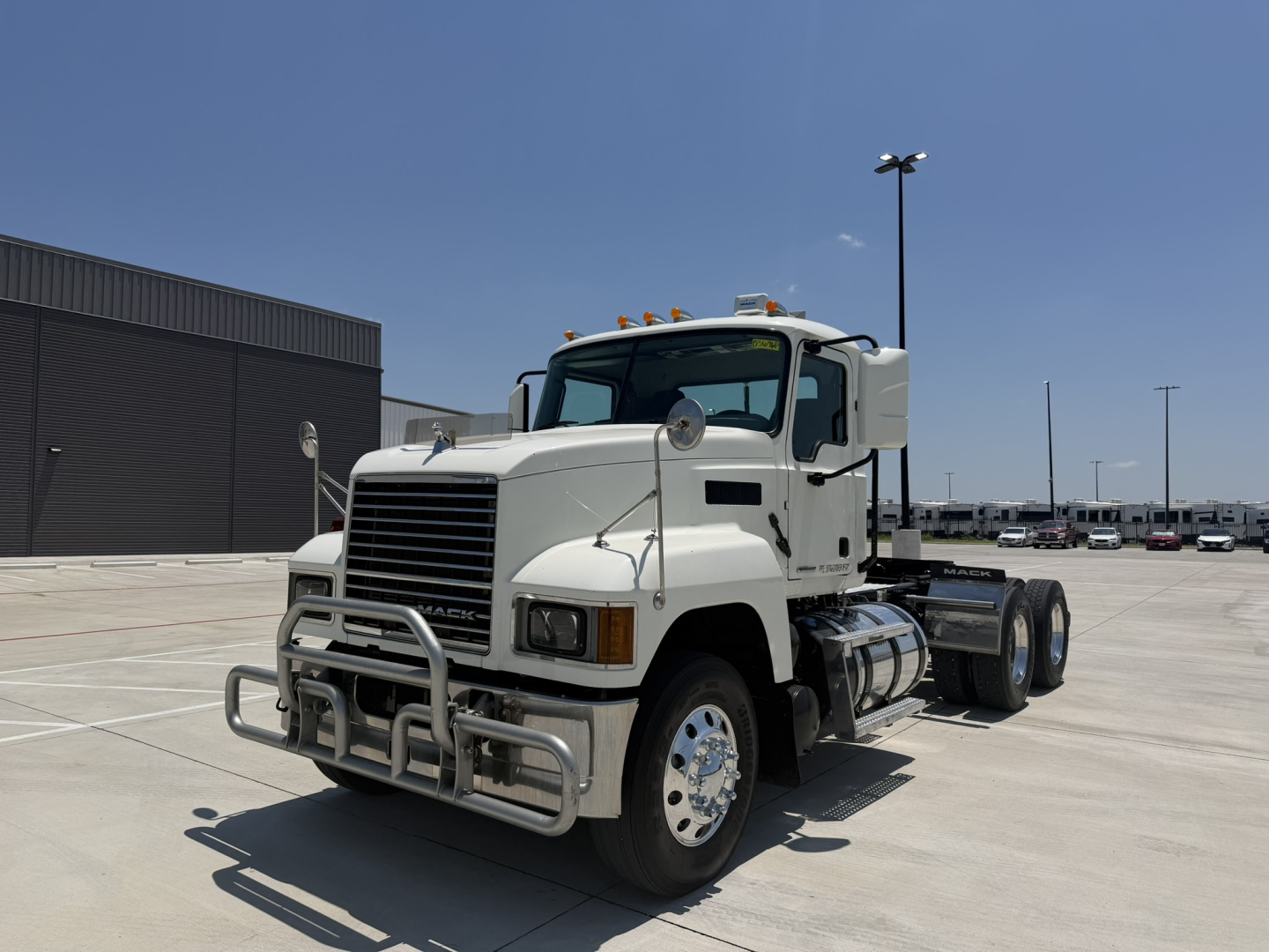 Mack PI64T conventional daycab truck in a parking lot showing front grille and bumper guard with chrome wheels.