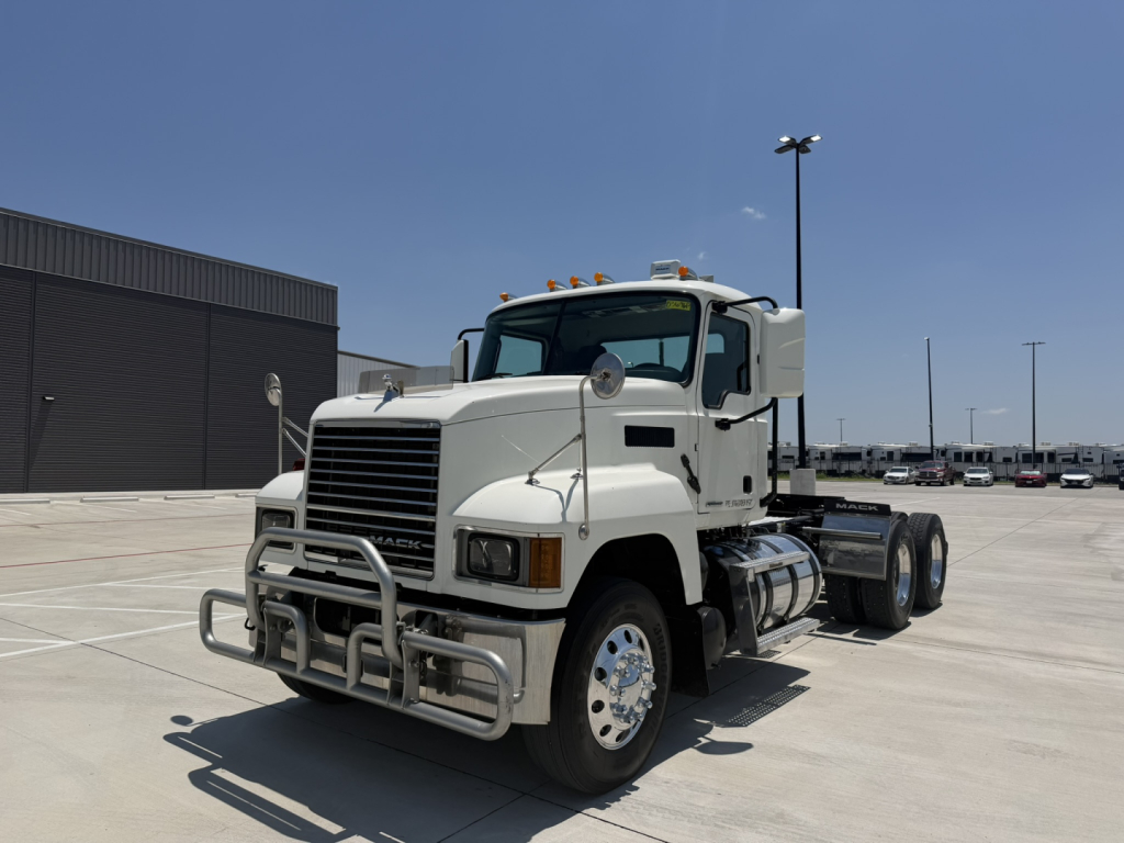 Mack PI64T conventional daycab truck in a parking lot showing front grille and bumper guard with chrome wheels.