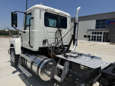 Truck cab and chassis of a 2020 Mack PI64T conventional daycab showing cab, fuel tanks, rear drivetrain, and exhaust stack with metal steps and wiring.