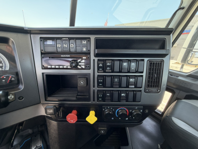Dashboard of 2020 Mack PI64T daycab showing gear selector, control switches, red and yellow knobs, and HVAC controls.