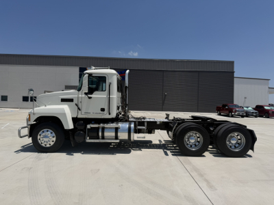 2010s white Mack PI64T tractor chassis side view with fuel tanks and dual rear axles, no trailer attached, truck yard background