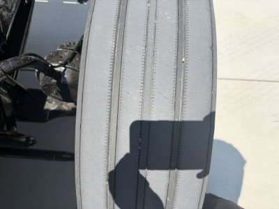 Front edge of a semi truck tire showing tread with shadowed area. No legible labels or numbers visible.