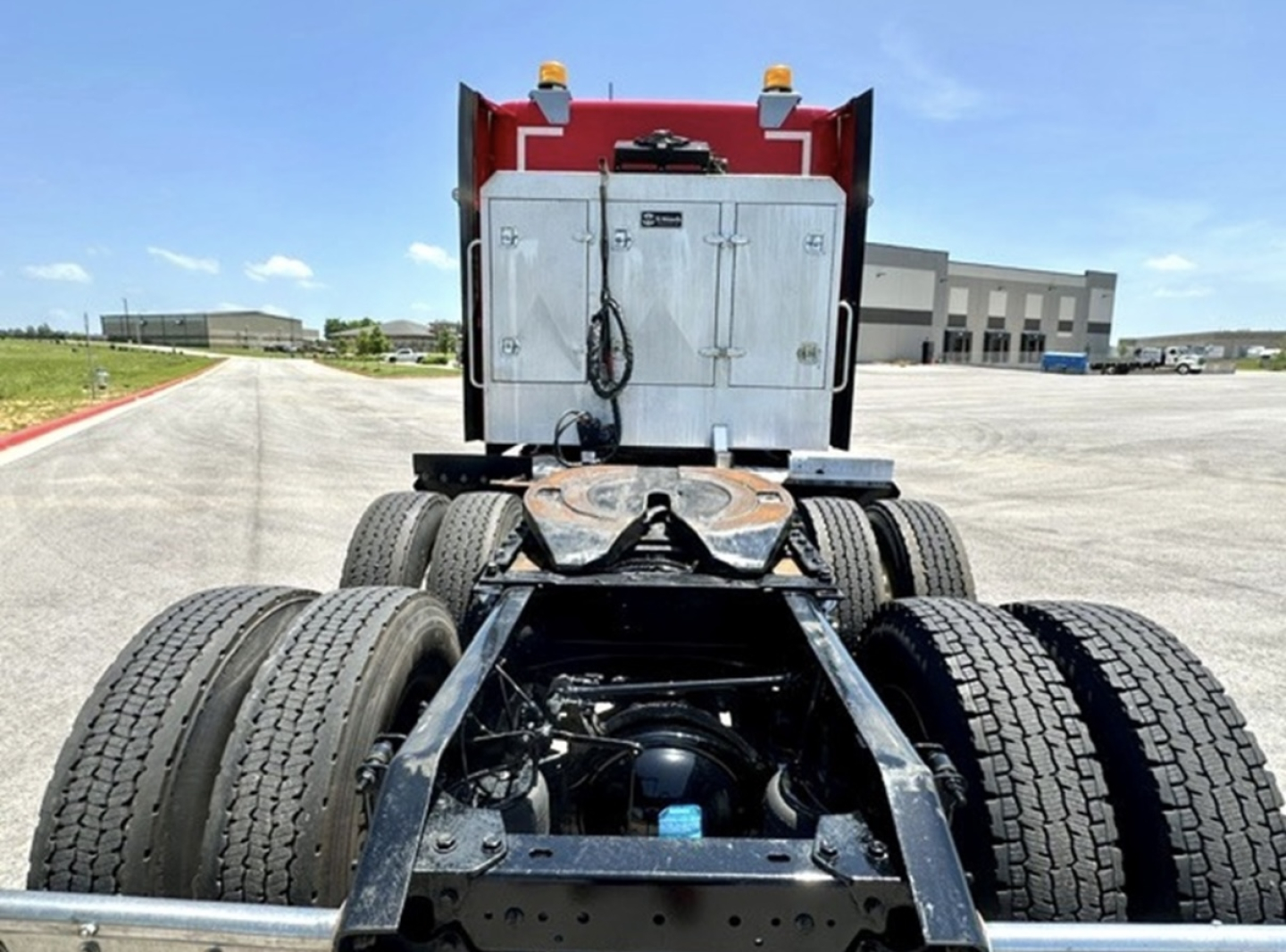 Kenworth T680 chassis rear view showing dual rear axles, fifth wheel area, and tool box; metal frame, tires, and rear cab with storage doors.