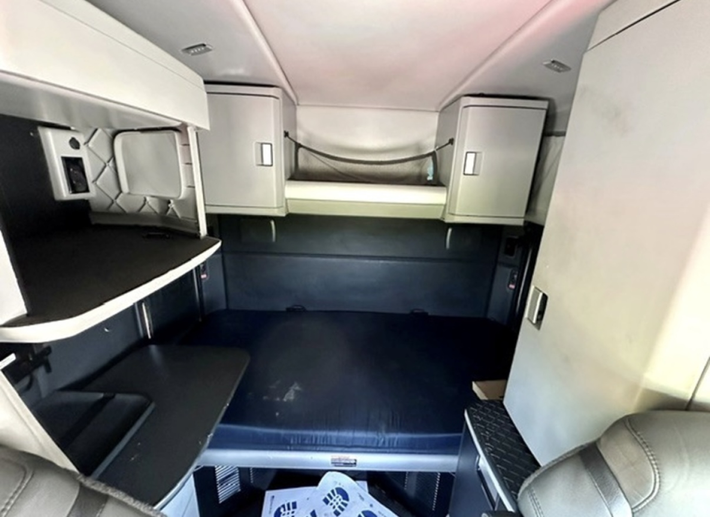 Kenworth T680 sleeper cab interior showing bunks and cabinetry with windowed storage and a dark floor