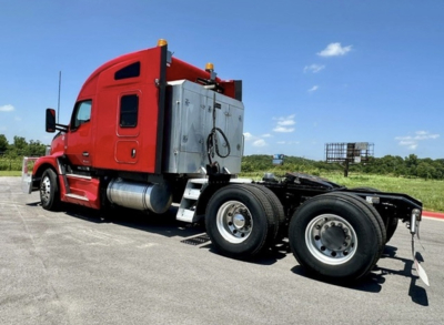 Kenworth T680 cab with red exterior and chrome fuel tanks, side view showing fifth wheel and rear axles, no text visible.