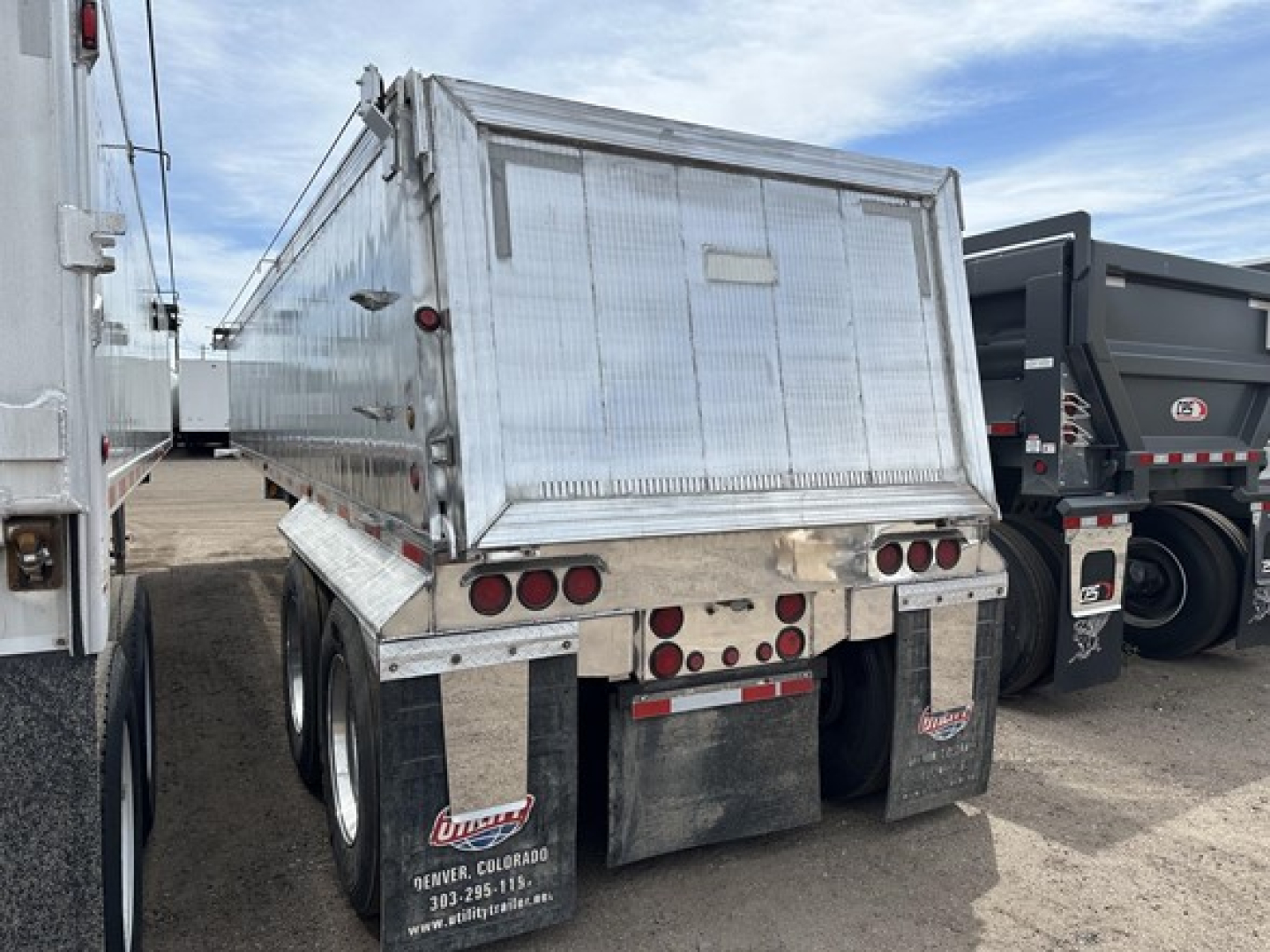 Dump trailer rear view showing aluminum dump body, dual rear axles, and taillight cluster with mud flaps.