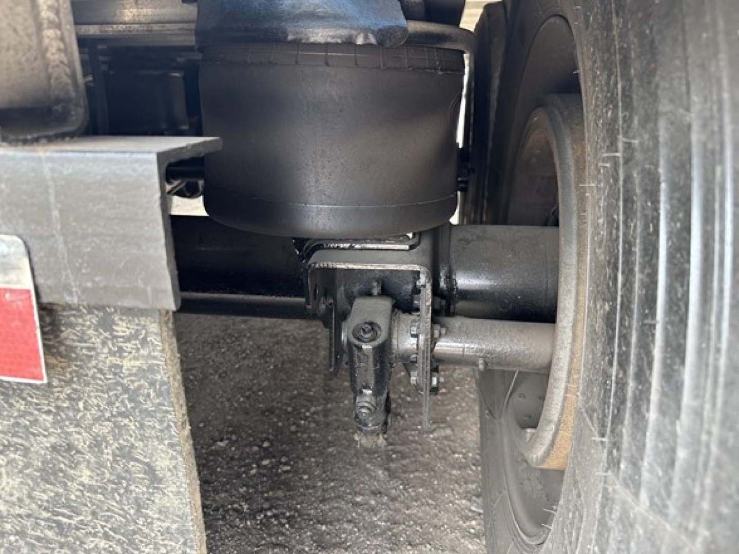 Dumper trailer undercarriage showing wheel, suspension, and air tank with connections; no legible brand names or model numbers visible.