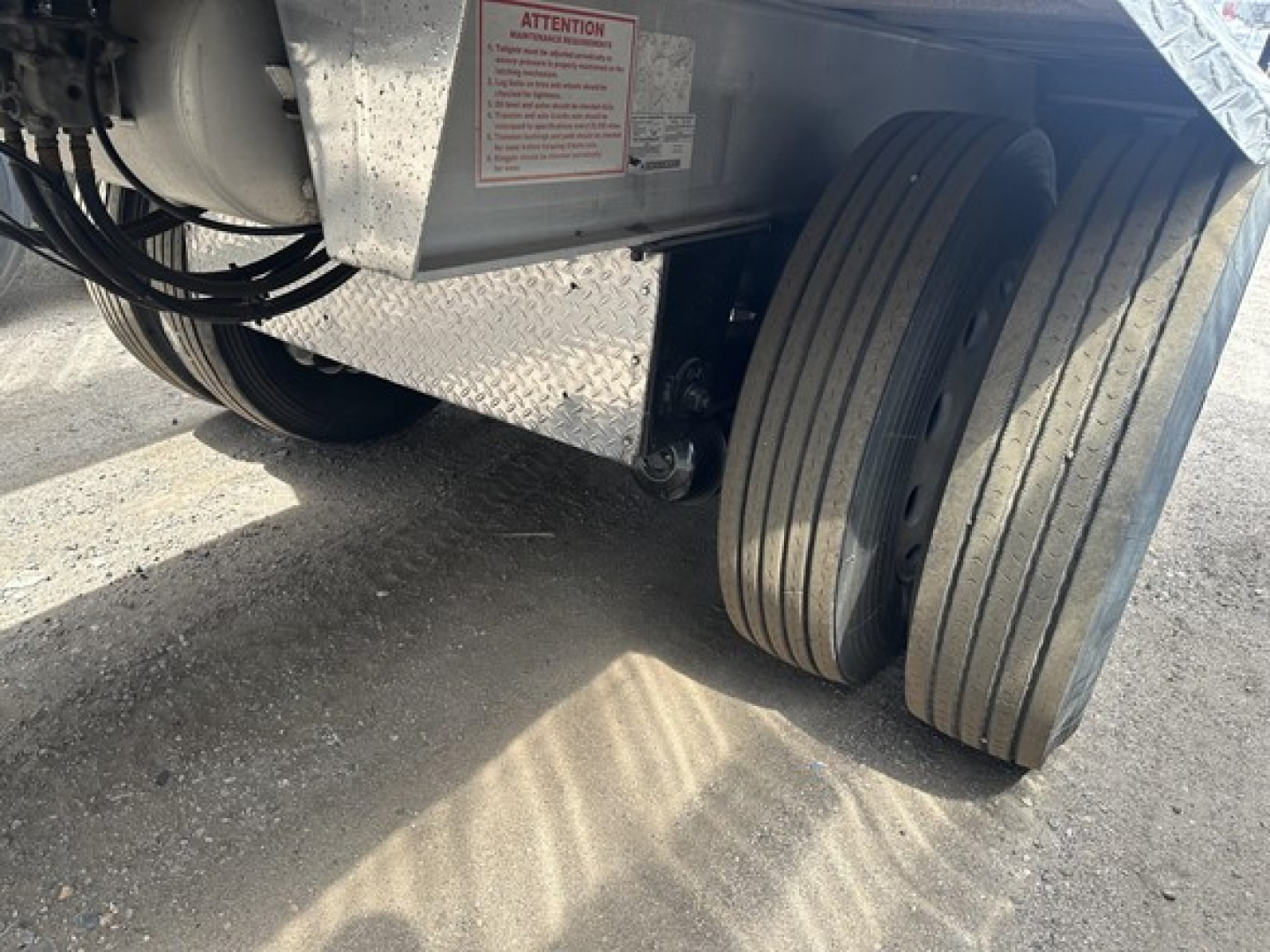 Dual rear trailer wheels and suspension area showing tire treads and frame with warning label.