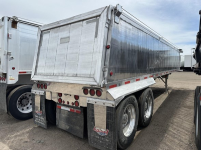 Trailer side view showing dump trailer with aluminum dump body and dual rear axles, chrome underbody, rear tail lights, and mudflaps.