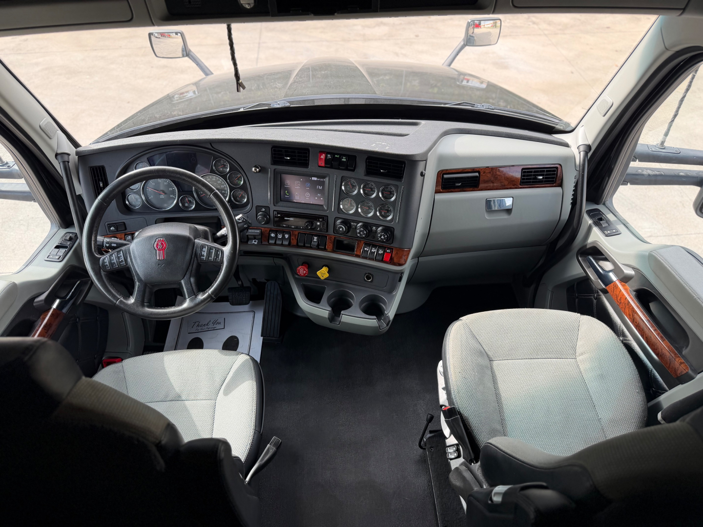 Kenworth T680 interior dashboard view with steering wheel, numerous gauges, center console, and dual front seats.