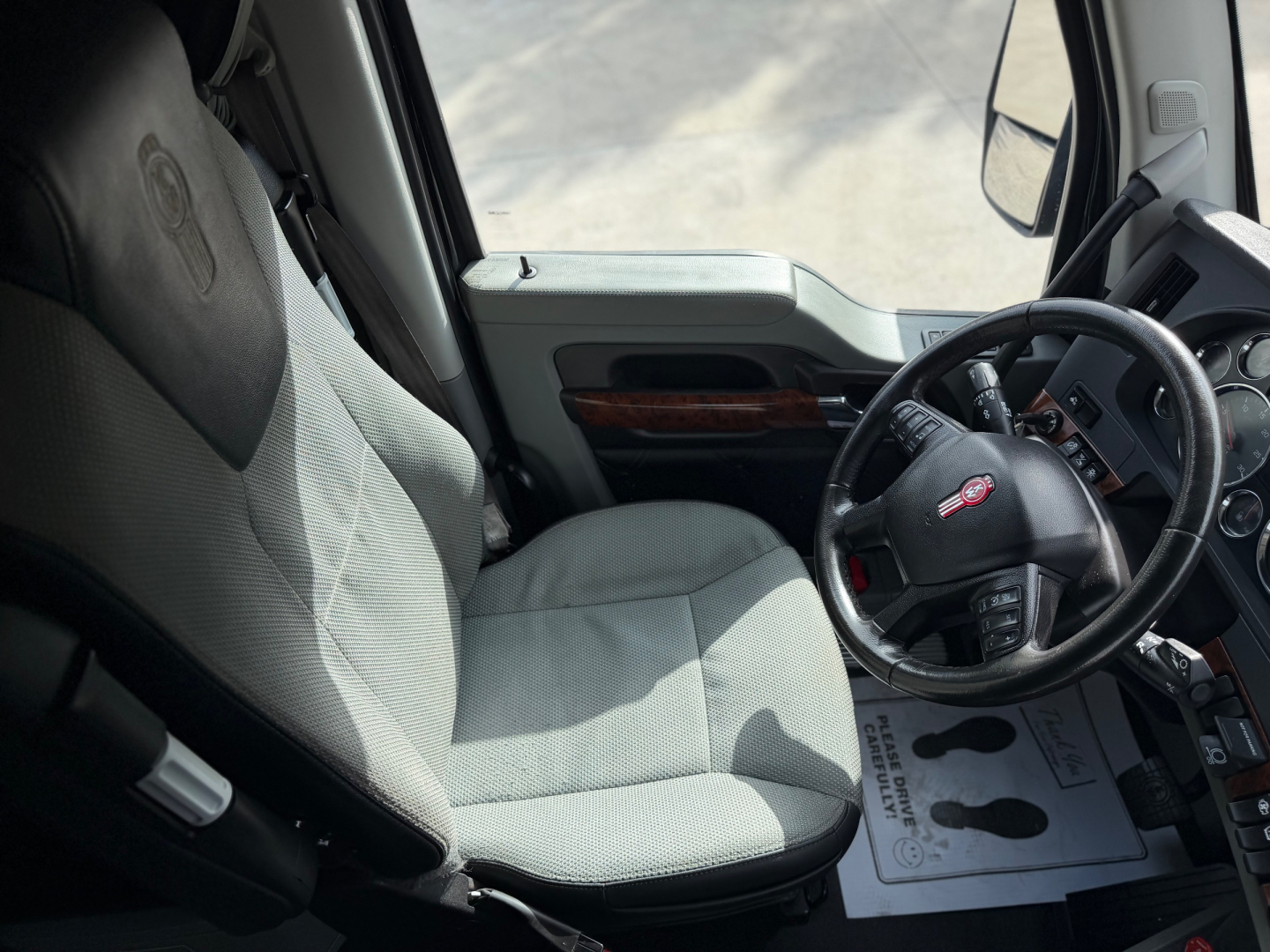 Kenworth T680 truck interior showing steering wheel and driver seat with light gray fabric upholstery.