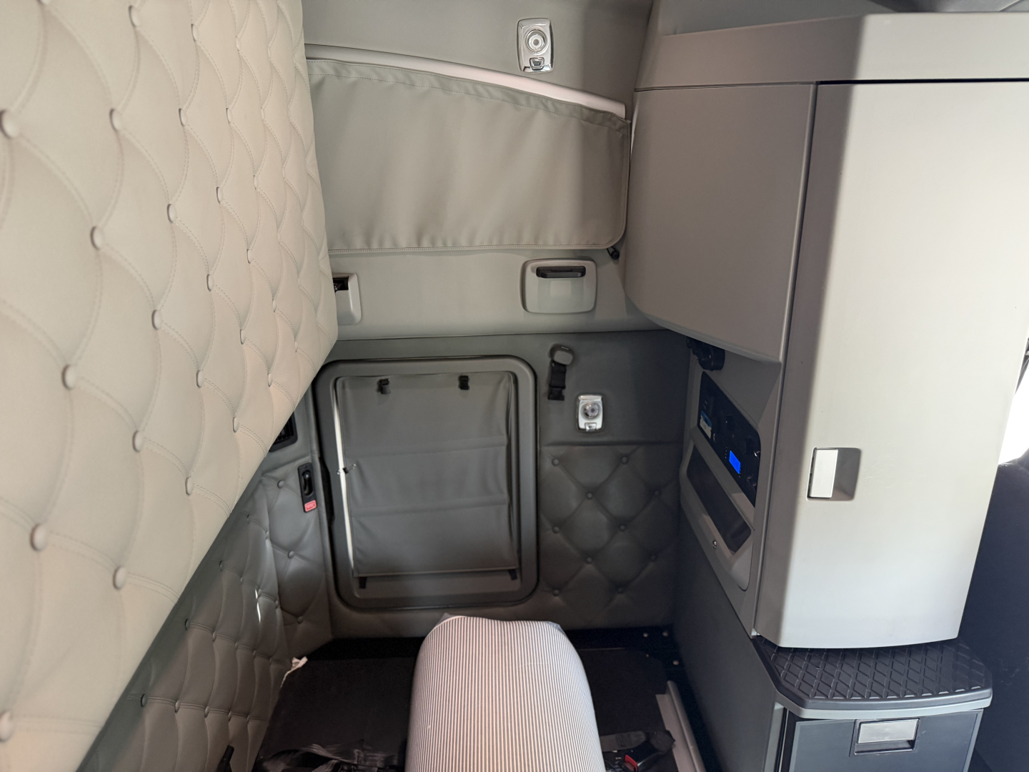 Interior of 2022 Kenworth T680 sleeper cab showing quilted light-gray upholstery, storage pockets, and cabau interior panels.