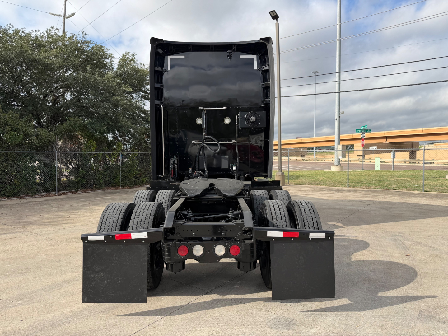 Kenworth T680 tractor rear view showing fifth wheel, dual rear axles, and mud flaps with chassis components visible.