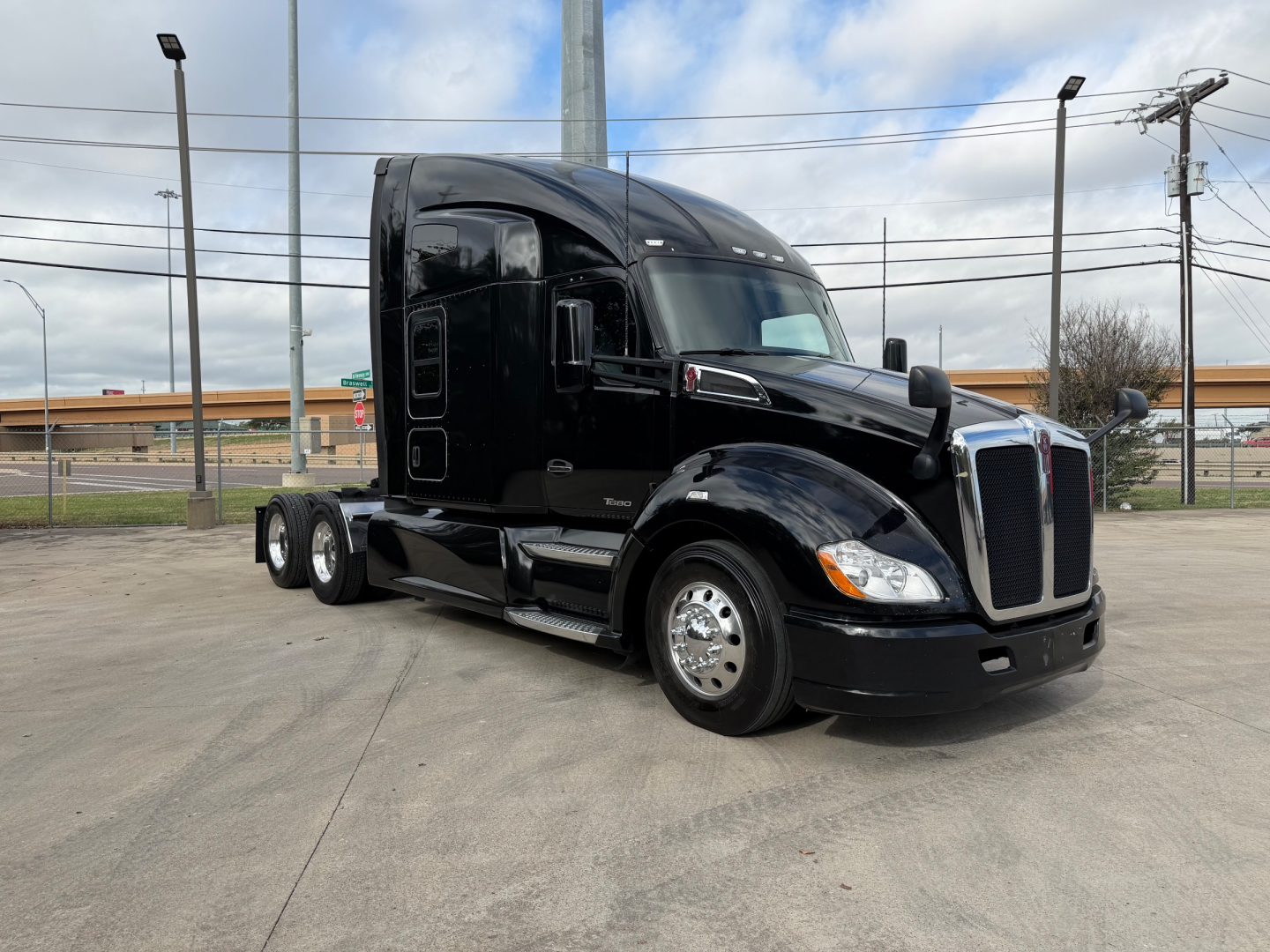 Kenworth T680 tractor with sleeper cab, black exterior, side view showing front grille and wheels.