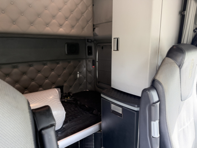 Kenworth T680 sleeper cab interior with quilted upholstery and storage cabinet, view from cabin area showing wall panels and seat.