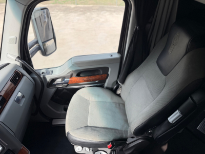Kenworth T680 truck cabin interior with gray fabric seat, steering area, and door panel showing wood trim and controls