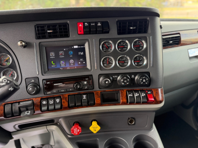 Dashboard cluster and center console of a Kenworth T680 showing a touchscreen infotainment system, multiple gauges, wood trim, and various control switches.