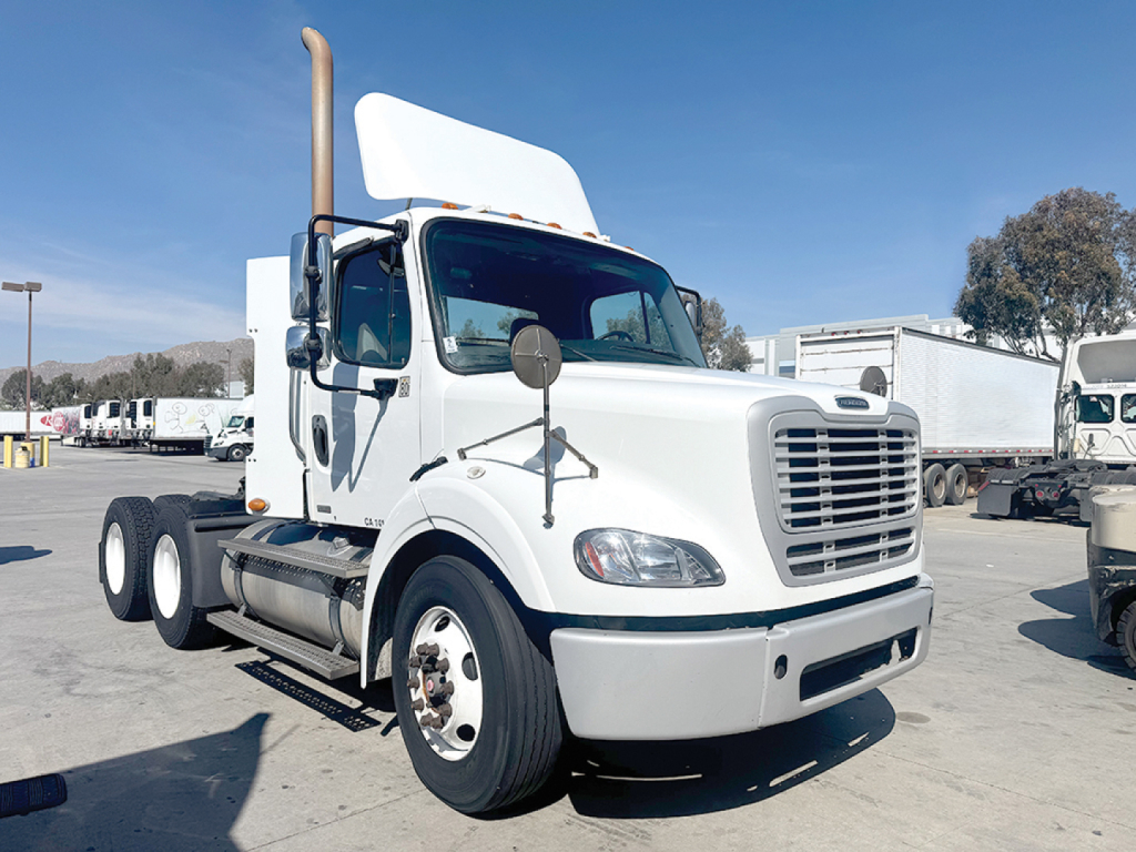 2012 Freightliner M2 112 conventional daycab truck front-left view showing large grille, dual rear axles, and side mirrors; VIN and stock info not shown on image.