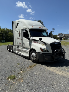 Freightliner Cascadia tractor in a parking lot with white cab and sleeper; visible decals on door and side; no legible model details beyond branding.