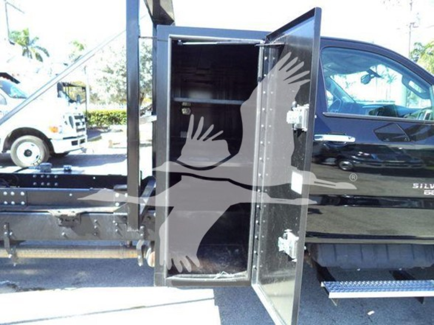 Truck cab with open storage cabinet showing interior shelves and latch, attached to a 2023 Chevrolet Silverado 6500HD rolloff truck.