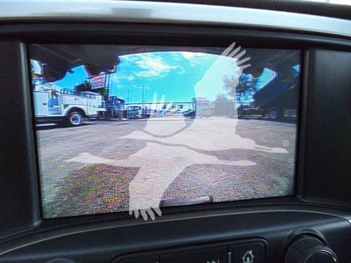 Truck camera display showing a view of a lot with service trucks and a faint overlay graphic.