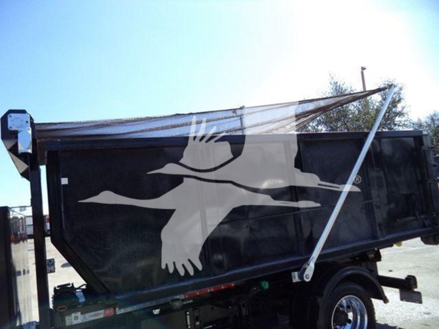 Dump truck bed with side panels and hydraulic mechanism showing a silhouette logo of a flying crane. No legible model text visible.