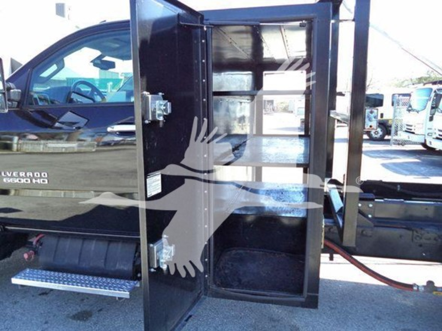 Truck side view showing open utility compartments of a 2023 Chevrolet Silverado 6500HD roll-off truck with black paint and chrome steps.