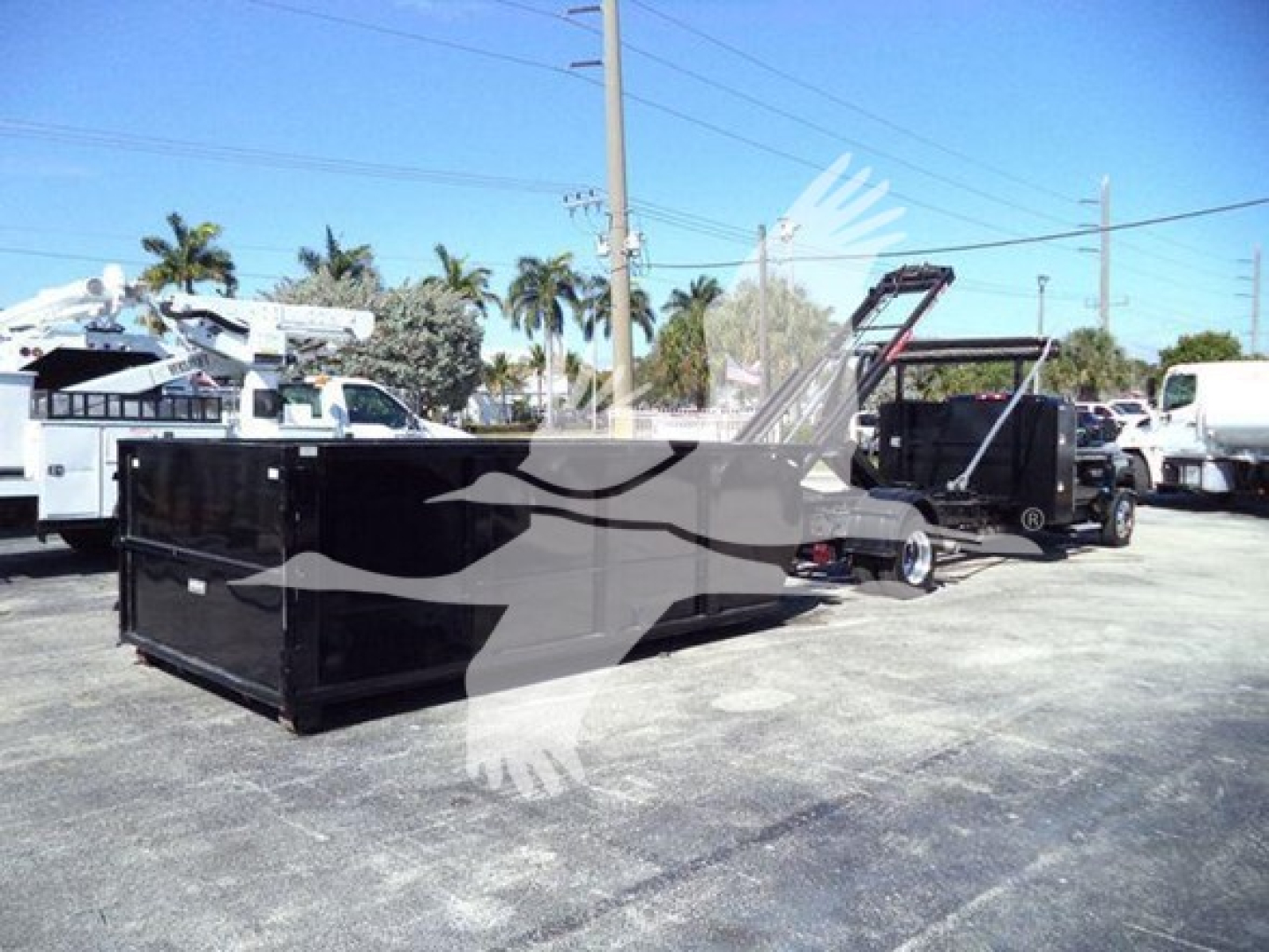 Dump truck with black trailer in yard showing roll-off bed and hydraulic hoist. No legible text visible on units.