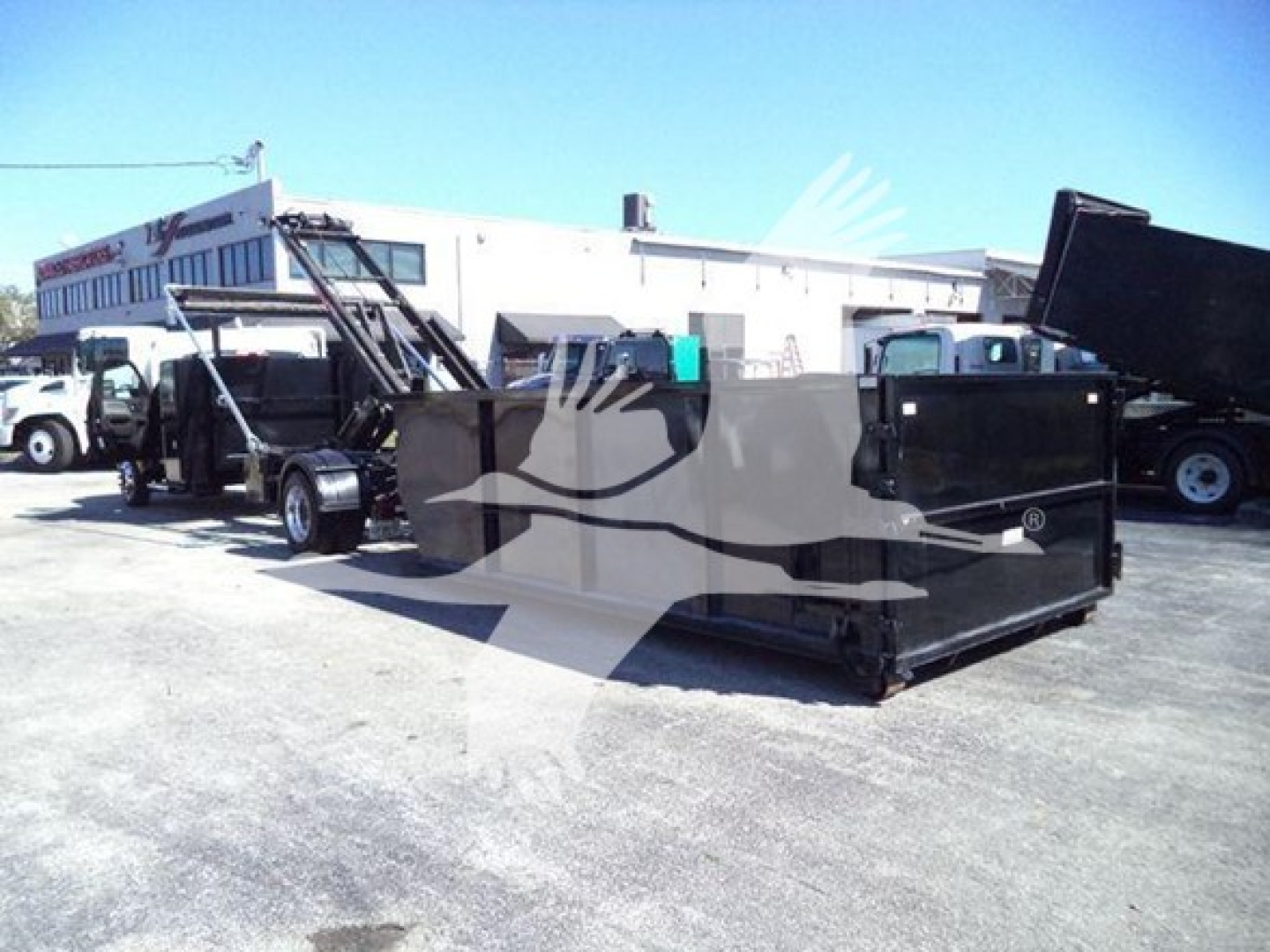Vehicle side view of a heavy-duty roll-off truck with a large black dumpster container attached; no legible model text visible.