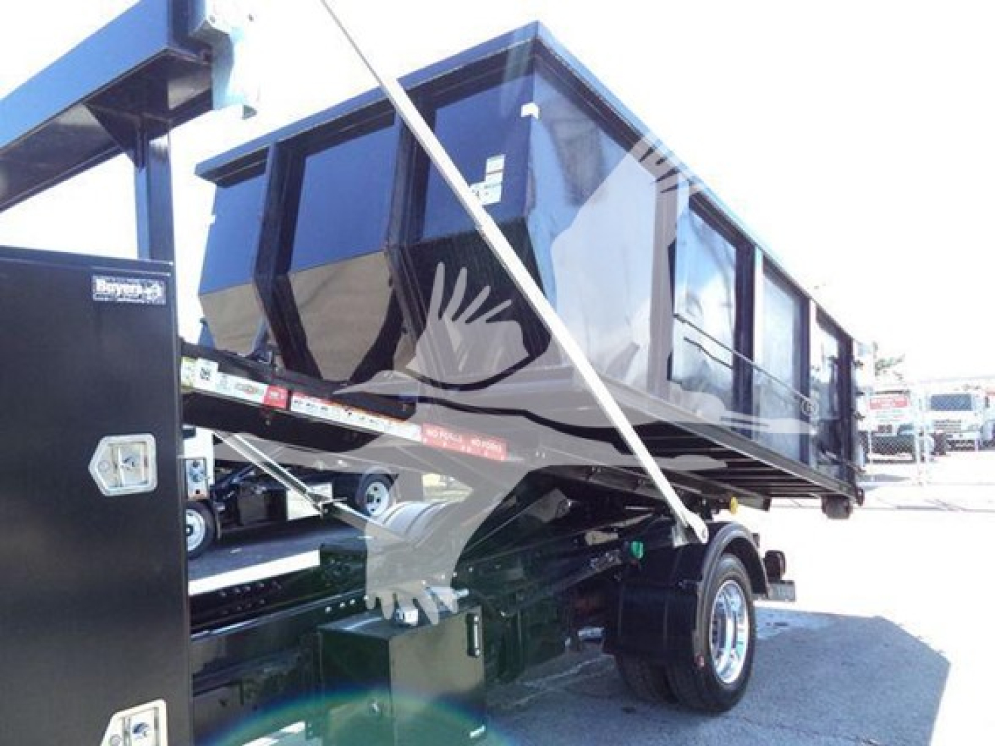 Truck bed/dump body on a Silverado 6500HD chassis showing roll-off dumpster trailer with black container and hydraulic mount. Visible VIN plate and stock tag obscured.