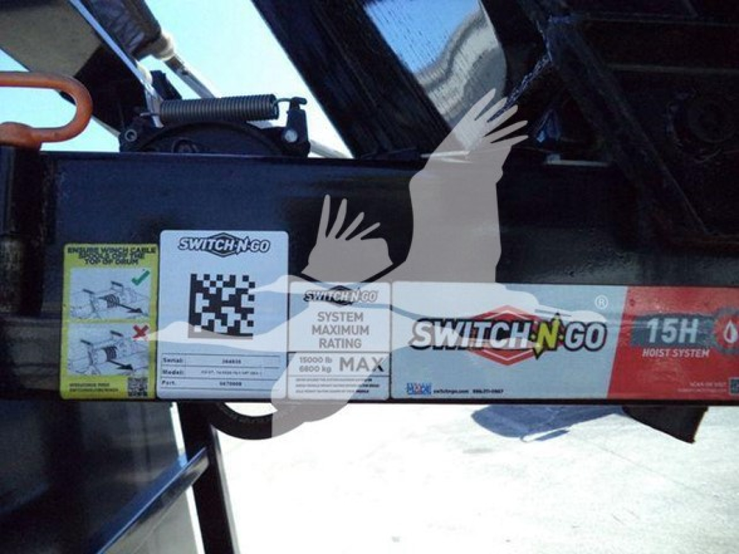 Dashboard label area with Switch-N-Go branding and QR code sticker, warning labels, and system max rating information on a black metal beam of a truck equipment attachment.