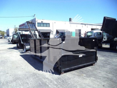 Dump truck bed attachment in a lot with other trucks and a building in the background.