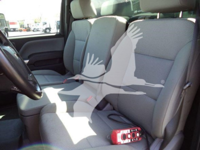 Truck cabin interior showing front seats and dashboard; seat upholstery light gray; small red device on passenger seat; window view of outside.