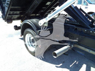 Truck bed and rear wheel of a 2023 Chevrolet Silverado 6500HD roll-off chassis showing exhaust pipe and undercarriage components.